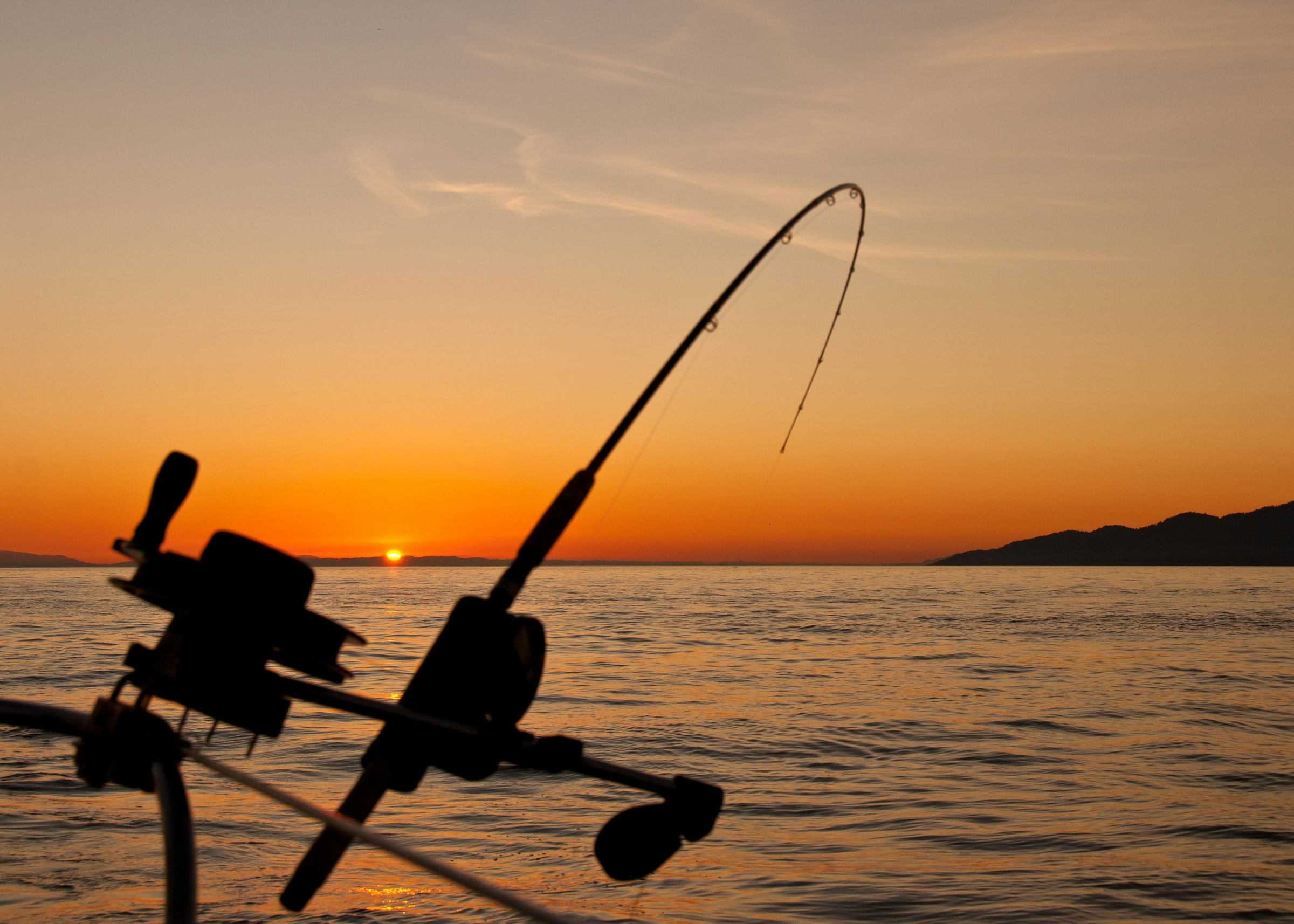 A fishing rod bent against the sunset over the Gulf of Mexico